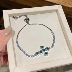 Nahaufnahme eines eleganten silbernen Kreuzarmbands mit grünen Zirkonia-Steinen