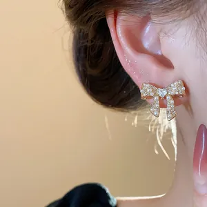 Close-up of elegant gold bow earring with pearls and heart crystal on ear