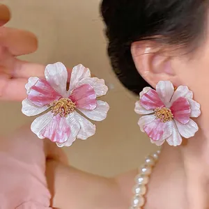 Orecchini a perno a fiore verniciato rosa e bianco alla moda sull'orecchio del modello