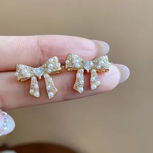 Close-up of elegant gold-plated bow earrings adorned with pearls and heart-shaped crystals