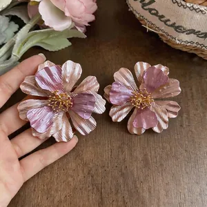 Orecchini a forma di fiore in metallo rosa e oro presentati su un fondo di legno rustico