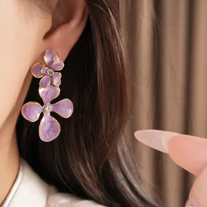 Detailed view of elegant purple enamel flower earrings with clear rhinestones on model