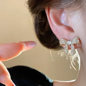 Detailed close-up of an elegant gold-plated bow earring with pearls and a heart-shaped crystal