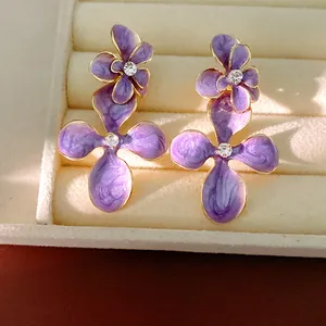 Detailed view of purple enamel flower stud earrings with sparkling rhinestones in a white box