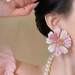 Primo piano di un orecchino a fiore rosa oversize con petali strutturati e oro