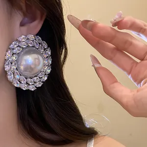 Close-up view of a large round pearl stud earring with zircon surround on the ear.
