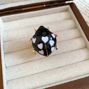 Close-up of black enamel ladybug ring with white heart patterns in jewelry box.