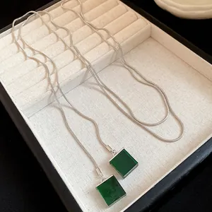 Detailed macro view of square green resin pendants on a silver snake chain necklace.