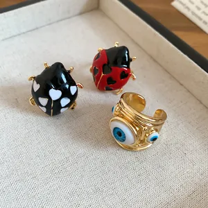 Close-up detail of enamel ladybug and gold evil eye open rings on a textured tray surface