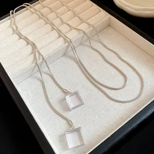 Macro detail shot of silver snake chain necklace with clear square resin pendants in a tray.