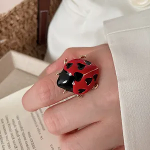Detailed view of red enamel ladybug ring with black heart patterns on model's hand