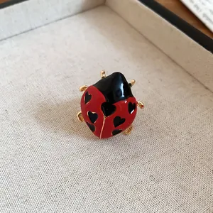 Close-up view of a cute red ladybug ring with black heart patterns and gold finish.
