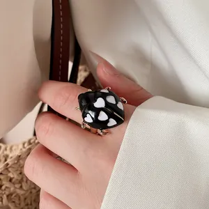 Close-up of a cute ladybug ring with black and white heart patterns on a finger.