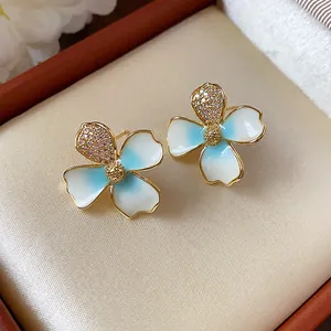 Dettaglio macro degli orecchini a lobo a fiore smaltati blu e bianchi con zircone