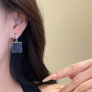Close-up of a vintage-style resin square pendant earring on a model.