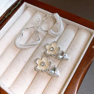 Detailed view of pearl-embellished heart hoops and floral earrings with crystal heart charms.