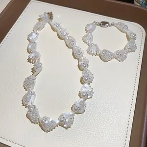 Elegant white shell and pearl necklace and bracelet set displayed on a cream jewelry pad