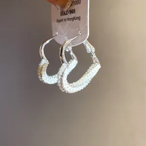Macro view of silver needle heart hoop earrings adorned with elegant small pearls
