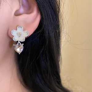 Detail shot of elegant silver needle flower and heart crystal dangle earring on model's ear
