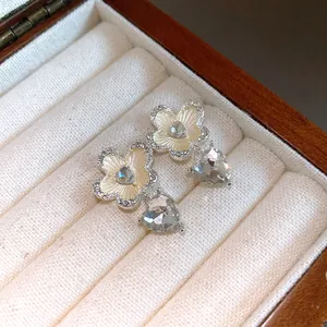 Close-up view of elegant silver flower and crystal heart drop earrings in a wooden jewelry box