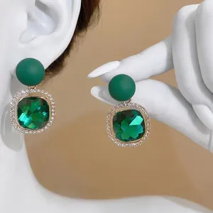 Elegant emerald green square stud earrings with a sparkling rhinestone border halo