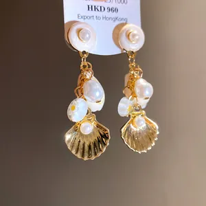 Detalle de pendientes colgantes dorados con perlas, conchas y flores blancas finas