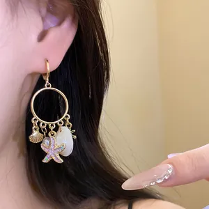 Detalle de un pendiente de aro dorado con dijes de concha y estrella de mar rosada.