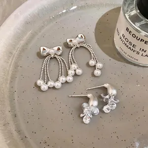 Elegant Korean style silver needle bow pearl tassel earrings on a textured ceramic tray