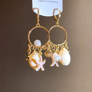 Detalle exquisito de pendientes de aro dorados con colgantes de perlas y conchas de mar
