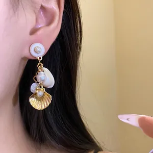 Primer plano de elegantes pendientes de perlas y conchas doradas para vacaciones en la playa.