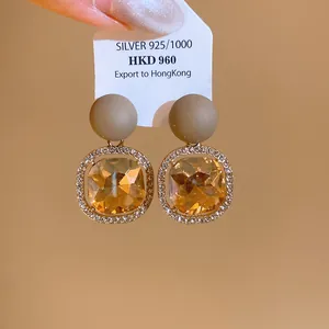 Detail of champagne crystal earrings with gold-tone frames and khaki matte studs