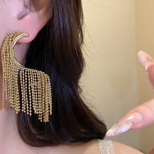 Detalle macro de elegantes pendientes dorados en forma de media luna con borlas de cuentas