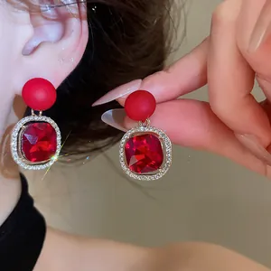 Close-up of elegant red gemstone drop earrings featuring a sparkling rhinestone halo detail