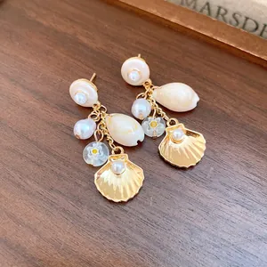 Detalle de elegantes pendientes colgantes dorados con perlas, conchas y flores.