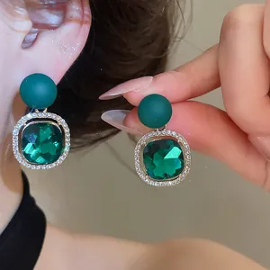 Close-up of elegant green gem earrings with sparkling rhinestone halo detail.