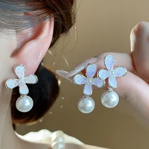 Primo piano di eleganti orecchini a fiore con perla indossati e tenuti in mano.