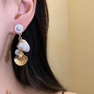 Elegantes pendientes colgantes de concha dorada y perlas lucidos por una modelo.