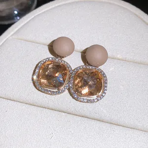 Close-up detail view of champagne gemstone earrings with diamond halo and matte studs