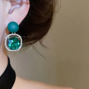 Close-up of a green gemstone earring with pavé rhinestones and a matte green bead.