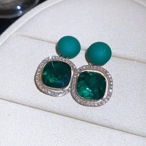 Close-up detail of emerald green square stud earrings with a sparkling crystal halo border