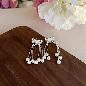 Close-up view of elegant silver bowknot stud earrings with flowing pearl tassels