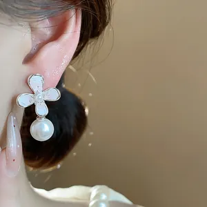 Dettaglio di un orecchino a fiore d'argento con perla pendente sul lobo dell'orecchio.