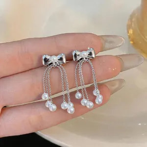 Detailed view of elegant silver bow earrings with delicate pearl tassels.