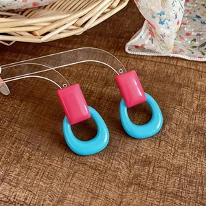 Detailed view of vibrant pink resin square stud and blue oval hoop earrings on wood