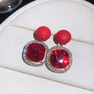 Detail view of luxury red gemstone stud earrings with sparkling rhinestone halo.