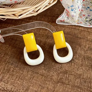 Close-up of minimalist yellow and white resin geometric earrings on a wooden surface.