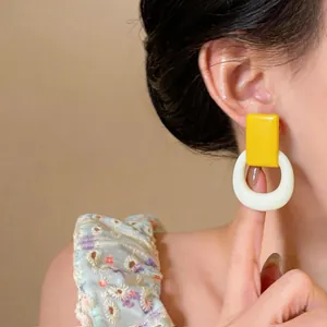 Close-up of yellow rectangular and white ring resin earrings on model's ear