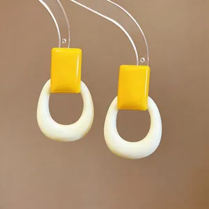 Macro detail of dopamine style yellow resin square and cream hollow hoop earrings