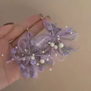 Dettaglio orecchini a fiore in raffia viola fatti a mano con perle e ago d'argento