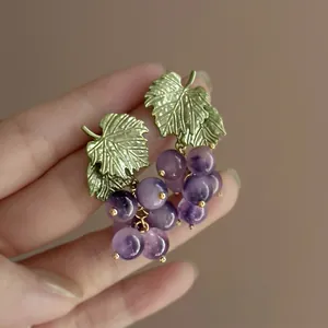 Primo piano di eleganti orecchini a forma di uva con perline viola e foglie verdi